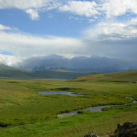 Looking toward snowy, cloud-covered mountains across a verdant valley crossed by river