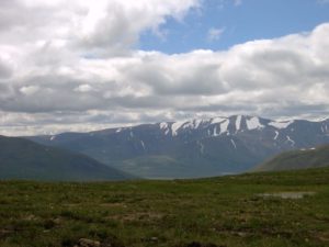 Old snow patches along a long mountain ridge. Sparse grass covers an flat area in the foreground