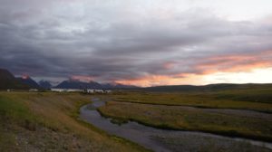 Sunset over a tundra-meadow valley. There's a camp in the rearground, along a low mountain slope.