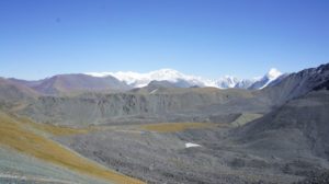 Featureless grey moutain ridges and glacial moraines with snow covered mountains in the background