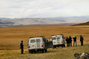 People standing around two vehicles in a wide steppe valley