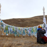 Traditionally-dressed person doing ceremony in front of ceremonial dyalama ribbons in Altai Republic