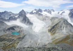 Multiple glacier tongues leading up to craggy mountain peaks. A small brilliant turquoise lake is visible.