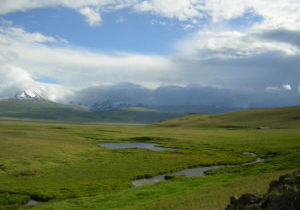 Looking toward snowy, cloud-covered mountains across a verdant valley crossed by river